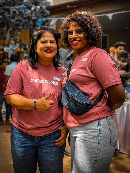 Two members posing for a photo at the Garage Sale. The pink 'Spokes Women' tee is a favorite in our community.