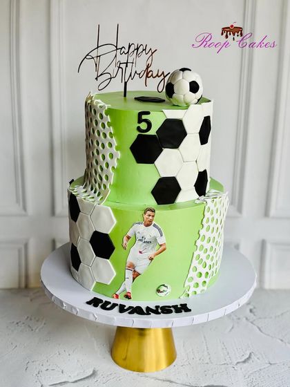 A fun football-themed cake for a 5th birthday. This two-tier cake is decorated with a soccer ball pattern, a net texture, and an image of a favorite player.