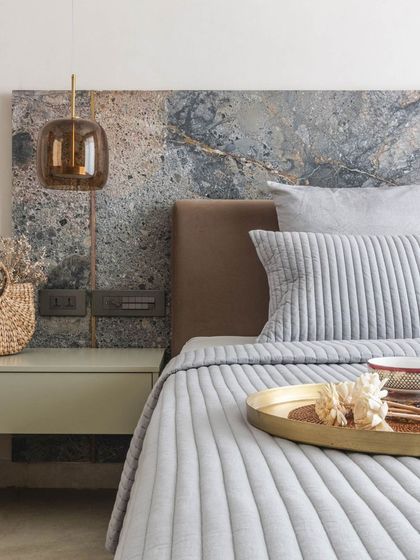This bedroom features a striking headboard made from a single slab of heavily-veined marble. Paired with soft blue-grey bedding and a glass pendant light, the look is both dramatic and serene.