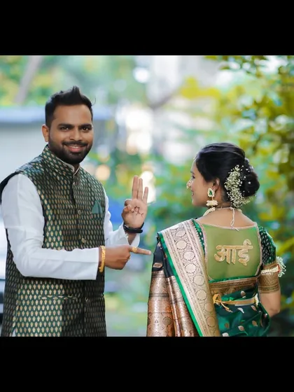 A playful outdoor portrait where the husband points to the 'Aai' (Mom) design on his wife's blouse, adding a touch of humor to their baby shower photoshoot.