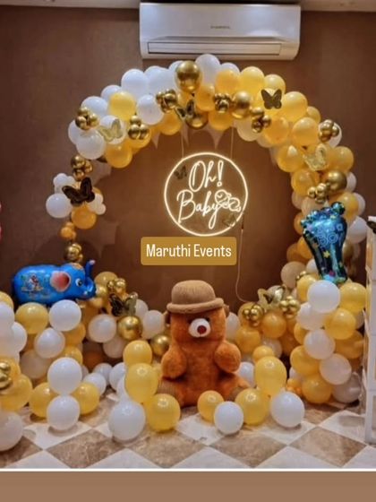 An adorable "Oh Baby" shower with a teddy bear theme. The yellow and white balloon arch is accented with gold butterflies, a neon sign, and cute props like baby feet balloons.