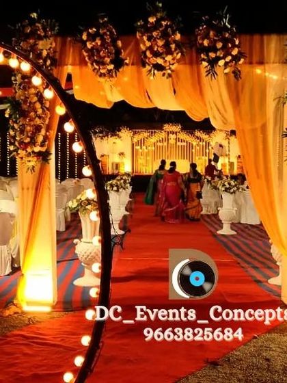 A grand entrance for an outdoor event, with a red carpet pathway, an illuminated circular arch, and warm, draped fabrics creating a celebratory walkway.