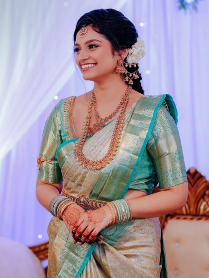 A candid shot of the bride's joyful smile during her engagement ceremony. She is dressed in a beautiful sea-green and silver silk saree.