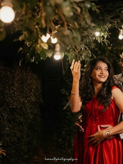 A candid moment during a night shoot, where a couple interacts playfully under hanging light bulbs in a garden setting.