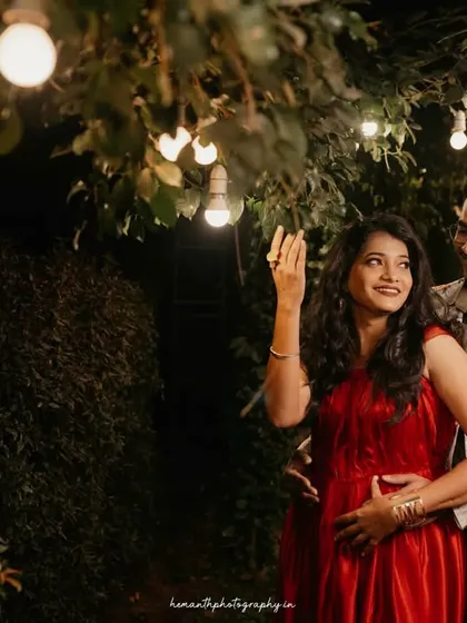 A candid moment during a night shoot, where a couple interacts playfully under hanging light bulbs in a garden setting.