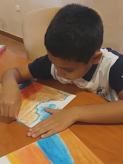 A student carefully blends oil pastels to create a beautiful sunset beach scene. This project teaches valuable lessons in color theory and blending.