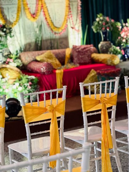 A view of the guest seating at the Mehendi ceremony, with white chiavari chairs decorated with bright yellow sashes, tying the whole look together.