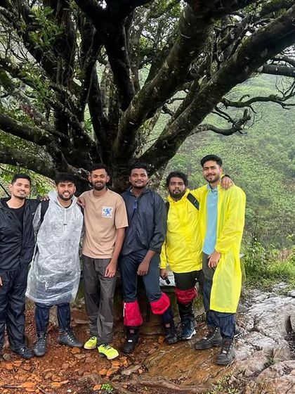 A group of friends, old and new, posing under a sprawling tree on a rainy day. Every trek with us tells a different story, but the people always make it unforgettable.
