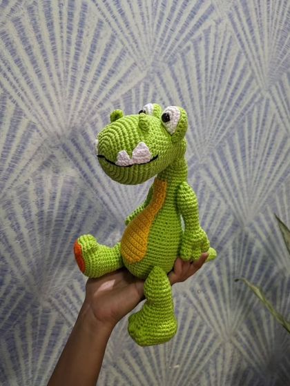 The crochet dinosaur sitting in my hand, set against a patterned wall.