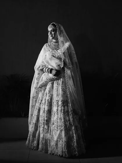 A dramatic black and white portrait of the bride, standing in stark contrast to the dark background. This shot emphasizes her form and the texture of her gown.
