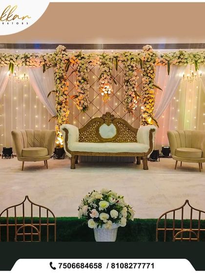 An elegant reception stage with a white and gold theme. The backdrop of white flowers and fairy lights, paired with a royal sofa, creates a timeless and sophisticated look.