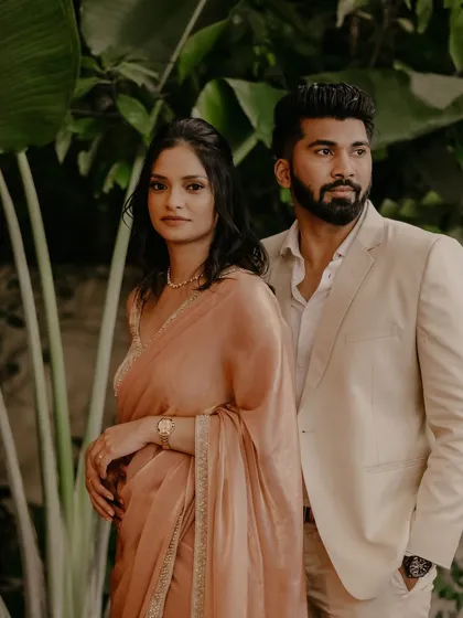 A stylish and poised portrait of the couple, showcasing their elegant engagement outfits against a lush green backdrop.