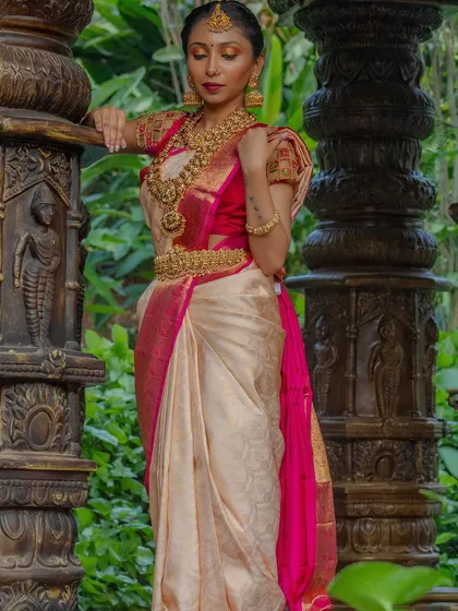 A model poses elegantly in a cream and pink silk saree, complemented by our heavy, layered temple jewellery set. The look is completed with a vaddanam and matching bangles.