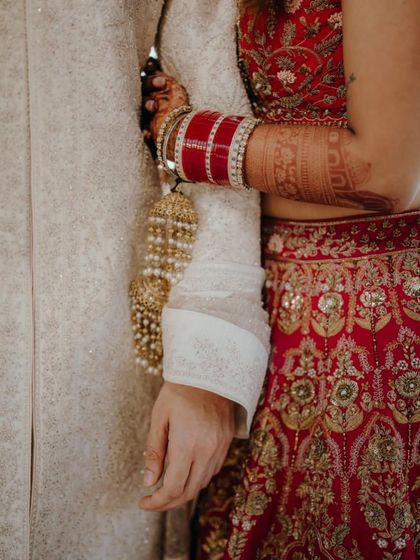 A close-up shot focusing on the details. The bride's mehendi, her red choora bangles, and her hand resting on the groom's arm all tell a story of love and commitment.