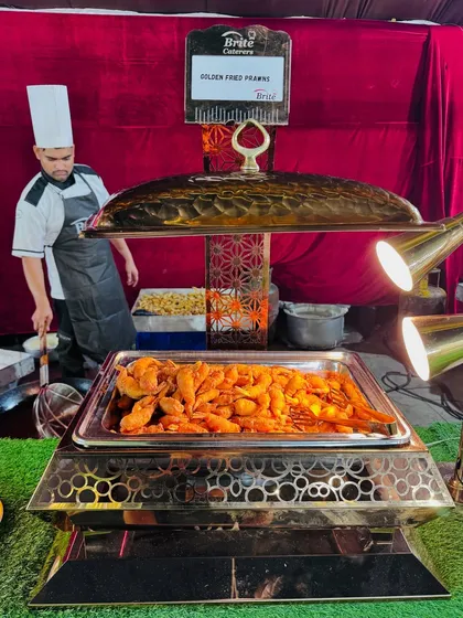 A chafing dish filled with golden fried prawns, kept warm under heat lamps, ready to be devoured.