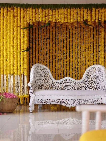 A stunning Haldi backdrop made entirely of hanging marigold garlands, with a beautifully carved white bench for the ceremony.