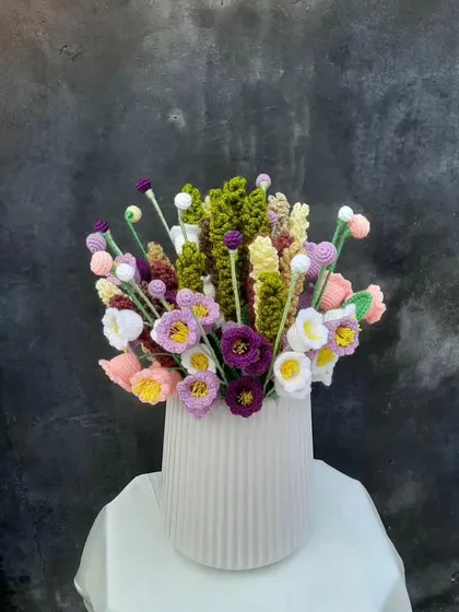 A full, vibrant bouquet of my crochet wildflowers arranged in a modern white vase. This piece includes a mix of purple, white, and yellow flowers with varied textures and green foliage, showing how my work can be a lasting centerpiece.