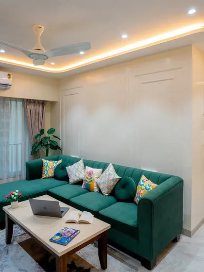 The comfortable L-shaped green sofa is perfect for family movie nights. The simple wall paneling behind it adds a touch of classic elegance.