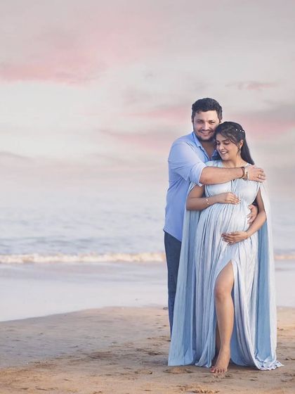 A quiet moment between a loving couple during their beach maternity shoot. The flowy cape and side slit of the blue gown create a soft, romantic look against the ocean backdrop.