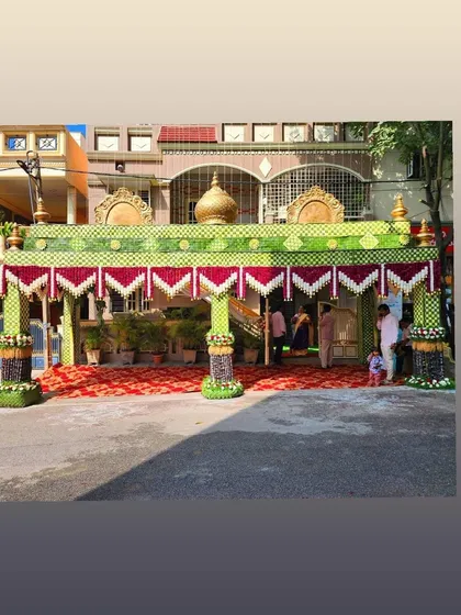 A wide view of a grand *chappara* setup for a wedding, covering the entire entrance of the house. The red carpet adds to the festive atmosphere.