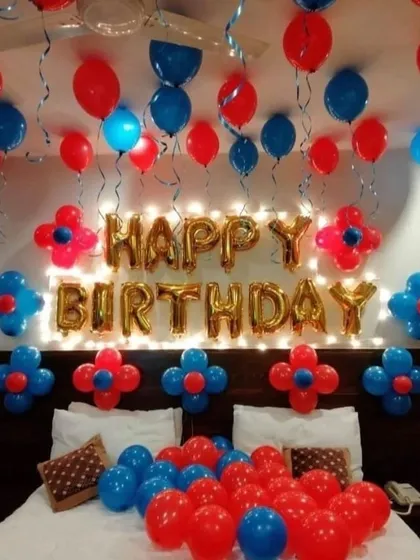 A simple red and blue birthday room decoration with foil letters, flower-shaped balloon clusters, and balloons on the bed.