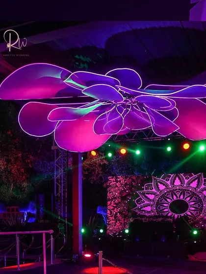 A large, flower-shaped neon installation hanging from the ceiling, bathing the dance floor in a purple glow. This is how I use lighting to create a massive impact.