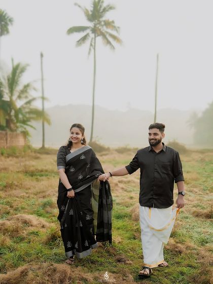 Walking hand-in-hand through a misty field with coconut trees in the background, a classic South Indian landscape.