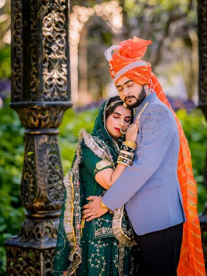 A couple in traditional Rajasthani attire shares an intimate moment between ornate pillars.