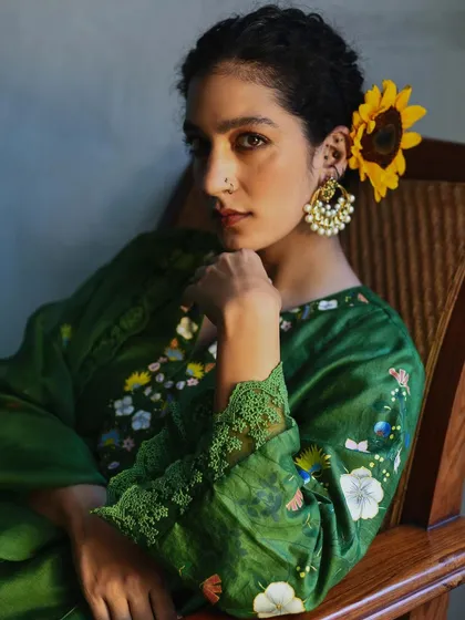 A close-up of a model wearing a green Baavli outfit, with a sunflower in her hair. The details are crisp and the mood is peaceful.