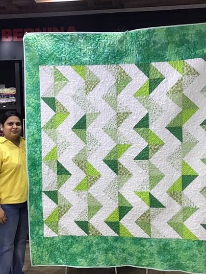 A happy client holding her large, green and white flying geese quilt.