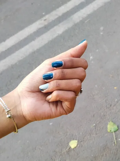 A still shot of the multi-toned blue manicure. The combination of dark teal, light blue, and a silver glitter accent creates a stylish and cohesive look on these short nails.