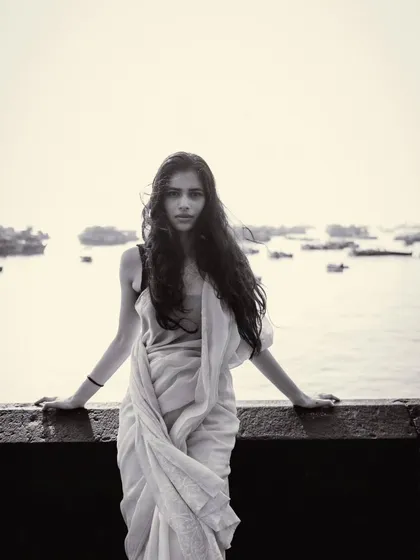 A beautiful, serene portrait in black and white, with the calm sea and distant boats creating a peaceful, almost ethereal backdrop.