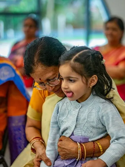 A grandmother holds her grandchild during the performance, sharing the experience across generations. It is a beautiful sight to see families coming together to be part of these cultural events.