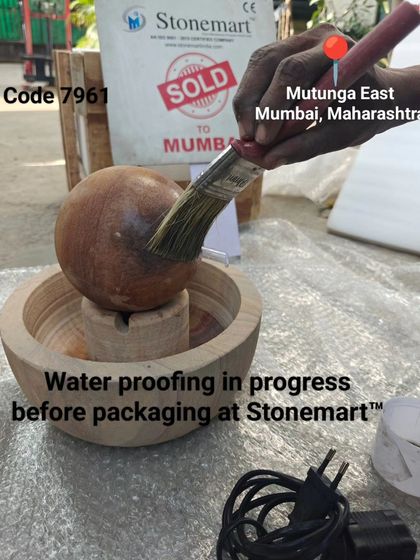 An artisan applies a waterproofing sealant to a small Rainbow Sandstone sphere fountain before it is packed for a client in Mumbai.