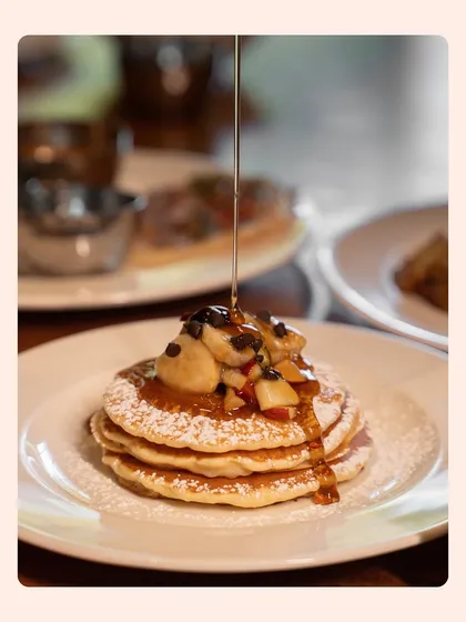 An irresistible action shot of maple syrup being poured over a stack of fluffy pancakes. This style of lifestyle food photography is incredibly effective at making viewers crave the dish.