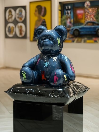 The "Ted – Ode To Keith Haring" sculpture, a deep blue resin form adorned with the artist's iconic figures. It sits on a glossy black cushion, a throne for a reimagined icon of pop art.