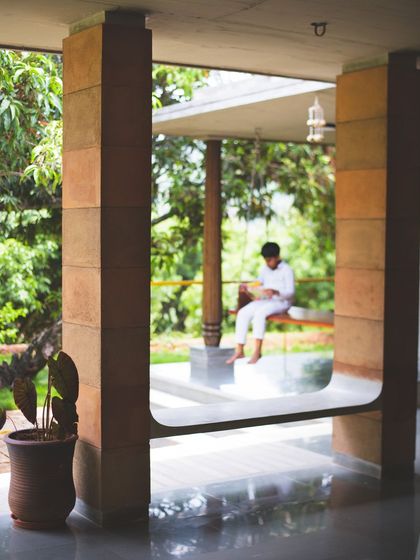A quiet moment on the verandah. The design of Aamra is filled with these "pause points," such as this integrated seat, which invite unhurried activities and a deeper connection with the serene surroundings.