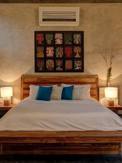 The bedroom of the private villa, featuring a custom wooden bed and wardrobe against a backdrop of textured cement walls. The artwork above the bed was specially commissioned for the project.