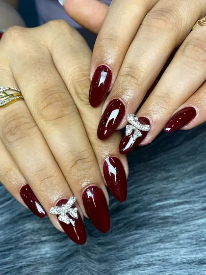 A classic and elegant look with deep maroon almond-shaped nails, accented by beautiful 3D rhinestone bow charms.