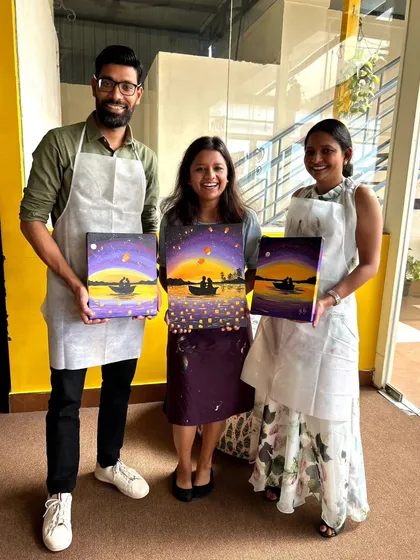 Three friends proudly displaying their matching sunset paintings. It's a perfect group activity to celebrate a special occasion or just a weekend.