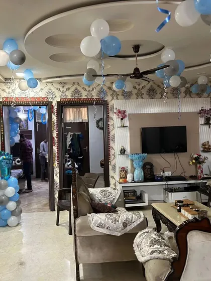 A full view of a living room decorated for a baby boy's welcome. The decor includes balloons floating on the ceiling and a balloon pillar topped with a baby foot shaped foil balloon.