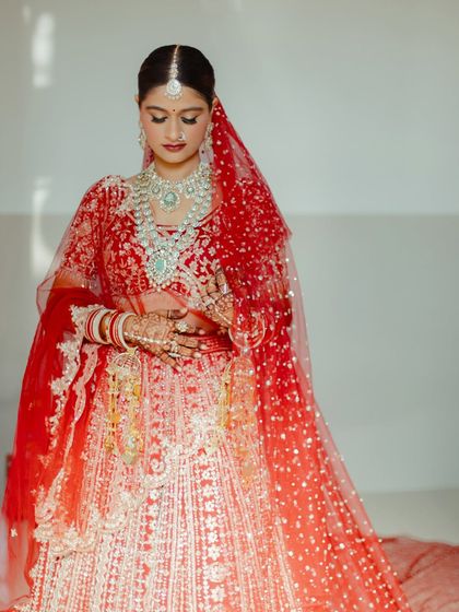 A classic bridal portrait. The focus is on her glowing skin, elegant jewelry, and the rich red of her lehenga, a timeless combination for any Indian bride.