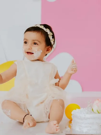 A close up shot showing her happy expression and the first bits of cake on her face. The soft lighting highlights her joyful mood.