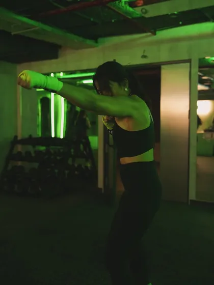 A client practices her jab-cross combination under the dramatic green lighting of "The Lab," our group class space.