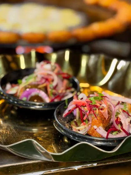 A beautifully plated serving of my Delhi style Karari Aloo Tikki Chaat. The crispy tikki is topped with yogurt, chutneys, and a garnish of fresh onions and beetroot, served in elegant black bowls.