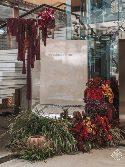 The welcome signage for the 'Orchard of Life' naming ceremony. A grand floral installation in rich, autumnal tones and cascading fabrics creates a warm and dramatic entrance for guests.