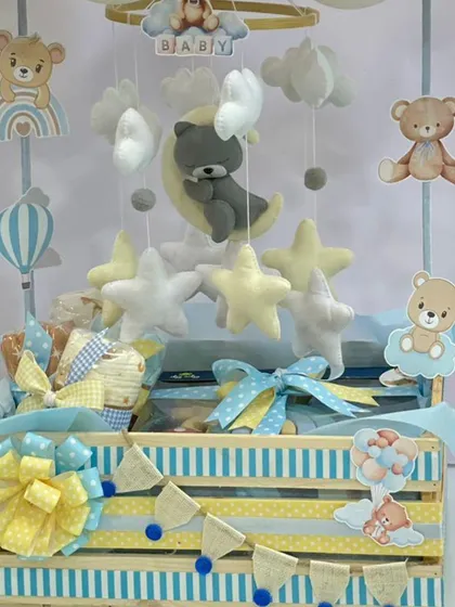 This teddy bear themed hamper features a charming mobile with felt stars and clouds, set in a blue and yellow wooden crate. It’s a sweet and classic choice for welcoming a baby boy.
