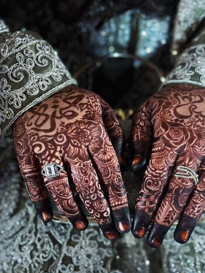 A professionally captured photo showing the beautiful contrast of the dark henna stain against the bride's ornate dress, with custom names adding a personal layer.