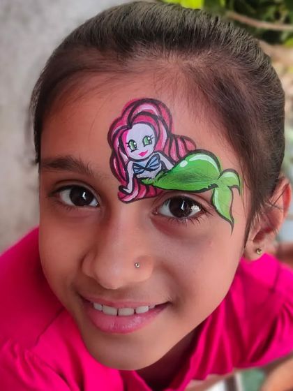 A cute mermaid design painted on a girl's forehead, perfect for an under-the-sea party.
