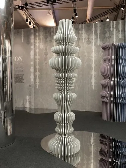 Sculptural totems made from layered, cut paper for the 'Silver Escapade' installation. These forms stand on a mirrored floor, creating infinite reflections and a dream-like, illusory dimension.